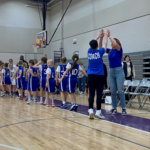 Members of the Girls Basketball team give end of game handshakes to the opposing team while coaches high five each other.